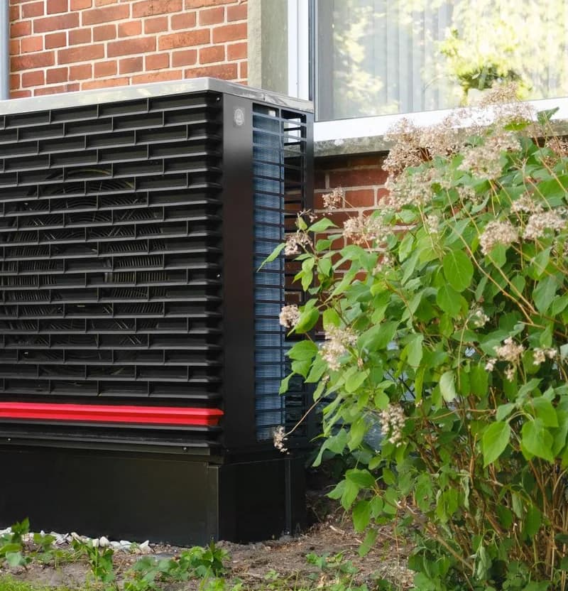 Modern residential outdoor air conditioner beside a brick home