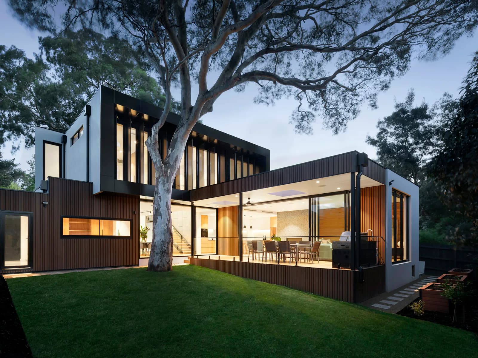 Modern two-story residence with wood and white cladding, lit from within at dusk