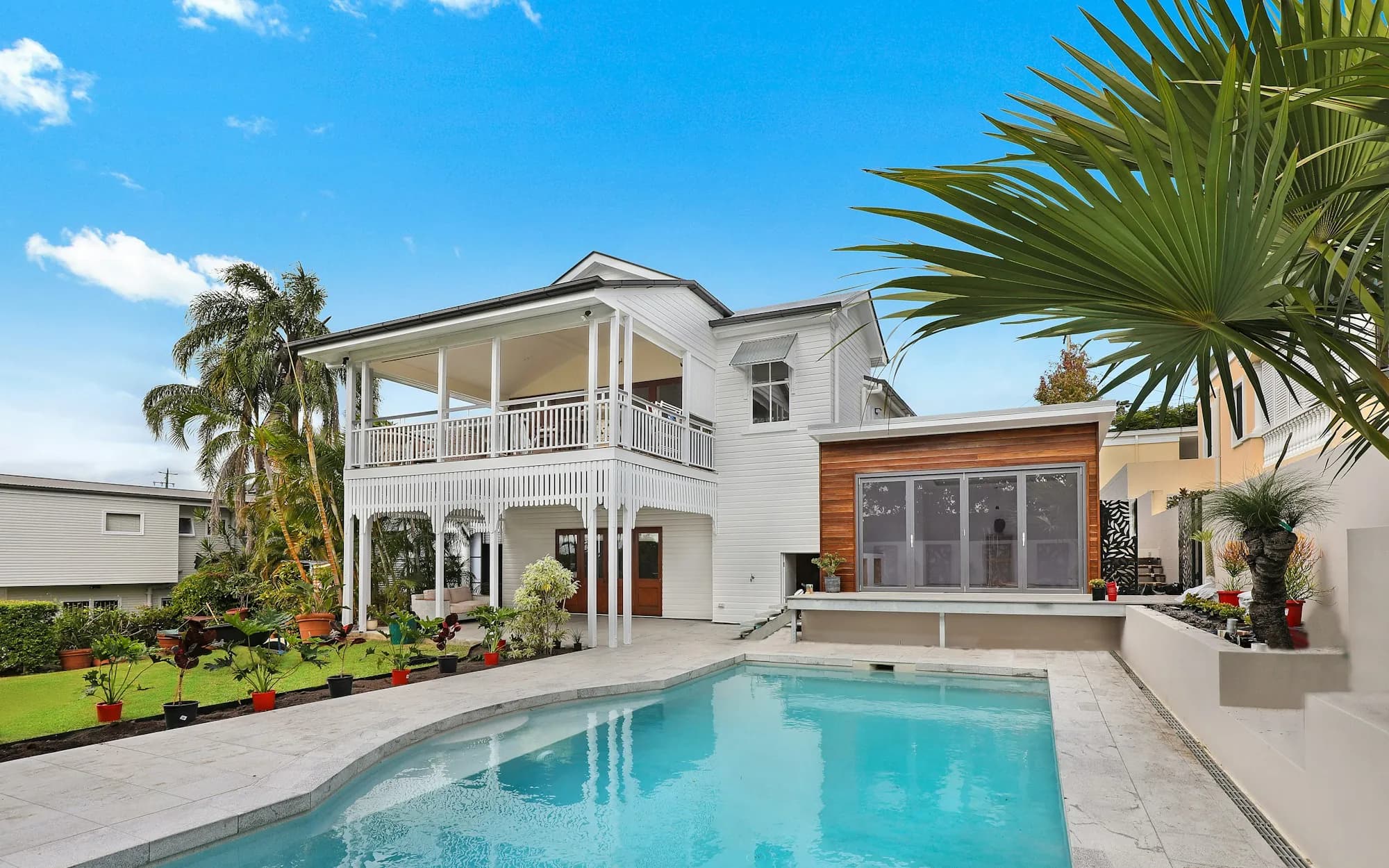 Modern white custom home with pool, wood accents, and palm trees in daylight
