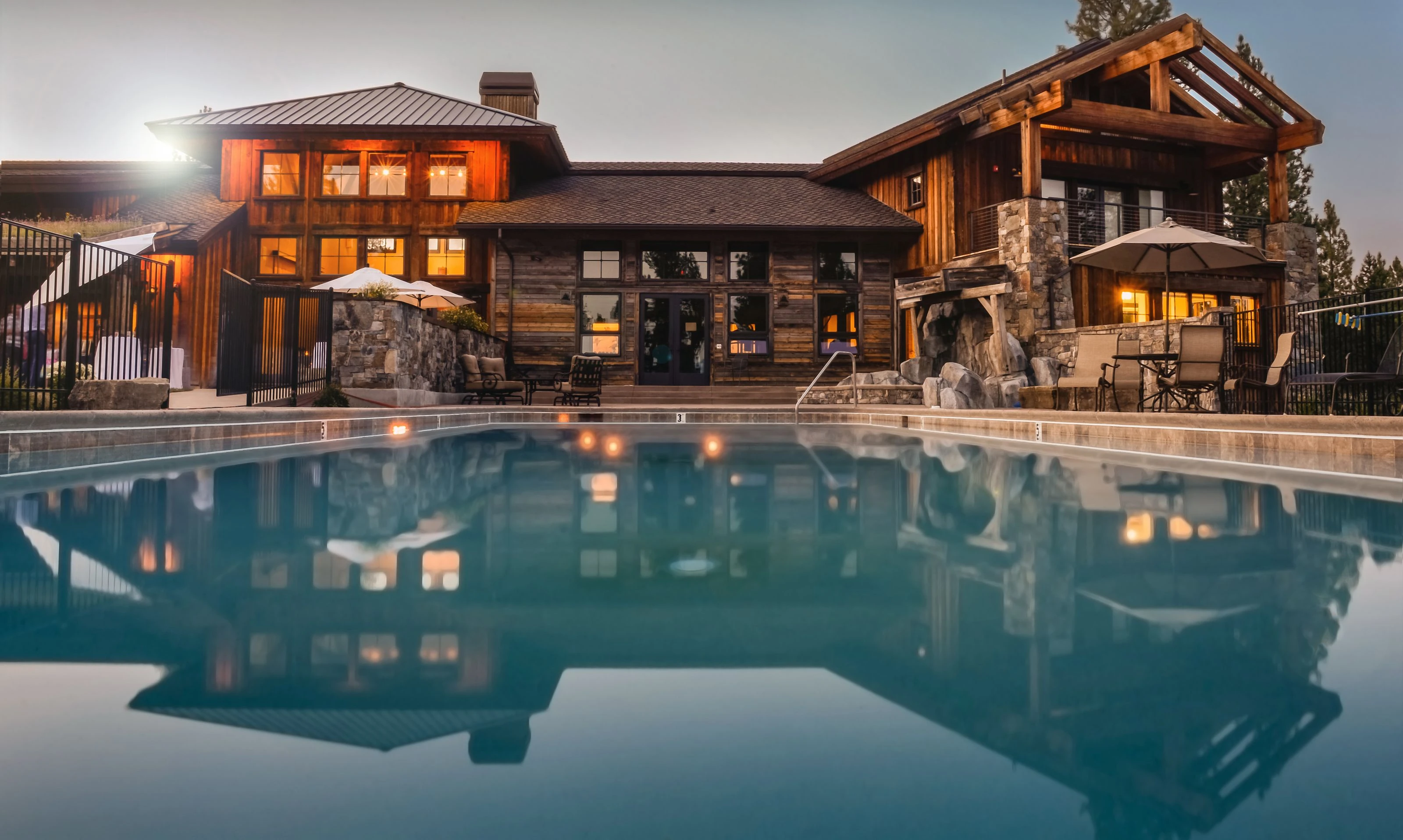Luxury modern residence at dusk with warm interior light reflecting across a still swimming pool